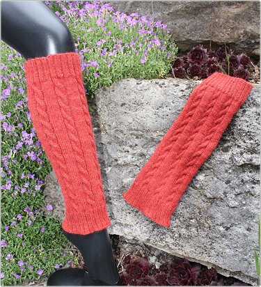 Koralle gestrickte Beinstulpen mit Zopfmuster auf Fels und Blumen