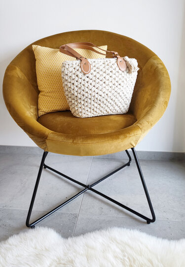 Boho-inspirierte gehäkelte Henkeltasche in Creme mit Quaste auf senffarbenem Stuhl