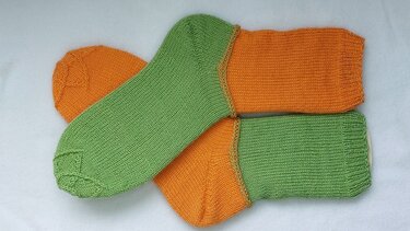 Zwei zweifarbige gestrickte Socken in Grün und Orange, übereinander liegend auf weißem Hintergrund