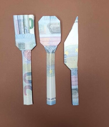 Gabel, Löffel und Messer aus gefalteten Euro-Geldscheinen auf braunem Untergrund