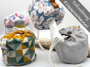 Mehrere genähte Klopapierbeutel aus gemusterten Stoffen mit Kordelzug und Griff