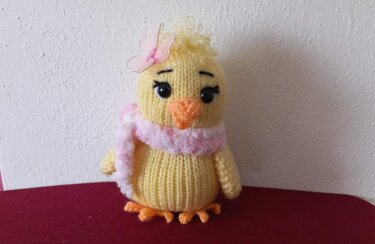 Gelbes gestricktes Amigurumi-Küken mit rosa Schal und Schmetterlings-Clip