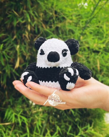 Kleines gehäkeltes Panda-Amigurumi in Schwarz und Weiß, in einer Hand gehalten, unscharfer Bambushintergrund