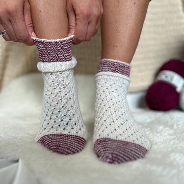 Weiße handgestrickte Socken mit feinem Lochmuster und weinroten Akzenten