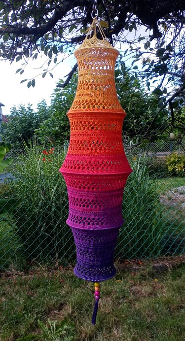 Mehrstufiger gehäkelter Hängelampion in Ombre-Farben von Gelb bis Violett, aufgehängt an einem Ast