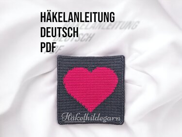 Quadratisches Häkelstück in Grau mit pinkem Pixel-Herz auf hellem Hintergrund
