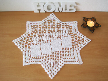 Weißes gehäkeltes Sternendeckchen mit vier Kerzenmotiven auf Holz, daneben ein Teelichthalter in Sternform und dekorative Buchstaben 'HOME'.