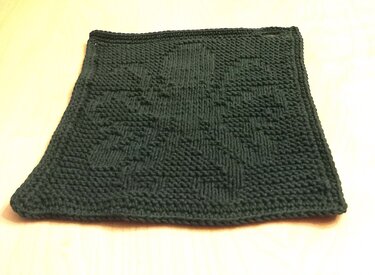 Dunkelgrüner gestrickter Topflappen mit erhabenem geometrischem Muster auf hellem Untergrund