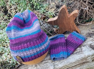 Gestreifte Strickmütze und passende Stulpen in Violett, Türkis und Grau auf Holzdeko