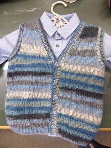 Gestrickte Babyweste mit horizontalen Streifen in Blau, Grau und Creme auf hellblauem Hemd