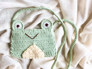 Hellgrüne gehäkelte Umhängetasche in Froschform mit applizierten Augen und hellem Bauch