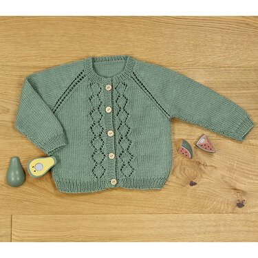 Mintgrüne Babystrickjacke mit Rauten‑Lochmuster, Raglanärmeln und hellen Holzknöpfen auf Holzuntergrund