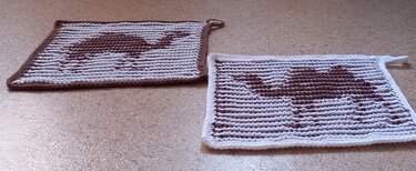 Zwei rechteckige gehäkelte Topflappen in Weiß und Braun mit Kamelmotiv und Aufhängeschlaufen