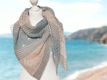 Gestricktes Dreieckstuch in Grau und Beige mit Streifen und Ajourmuster auf weißer Schneiderpuppe vor Meer