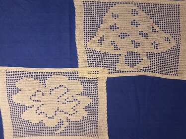 Zwei ecrufarbene, rechteckige Filet-Häkeldeckchen mit Blumenmotiven auf blauem Untergrund