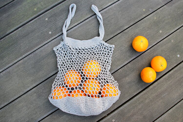 Gehäkelte graue Netztasche mit Orangen auf Holzplanken