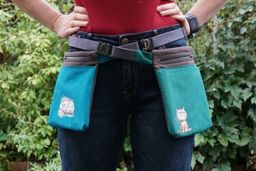 Person trägt doppelte Gürteltasche in türkis und grau mit Reißverschlüssen und Wohnwagen- sowie Katzenmotiv