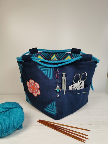 Dunkelblaues Stoff-Utensilo mit geometrischen Mustern, gefüllt mit Nähutensilien, daneben Garn und Stricknadeln.
