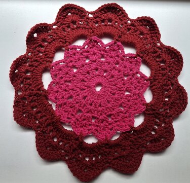 Round crochet coaster with pink center and burgundy scalloped outer edge