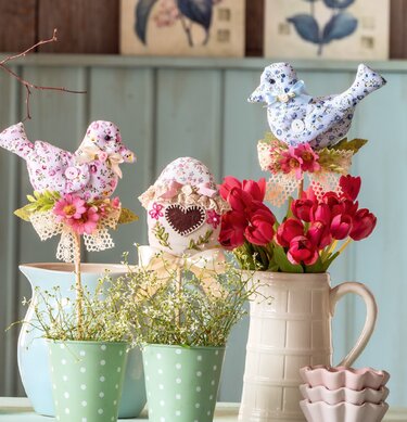 Zwei genähte Stoffvögel und ein verziertes Stoff-Osterei auf Holzstäben als Osterdeko in Vasen und Töpfen mit roten Tulpen