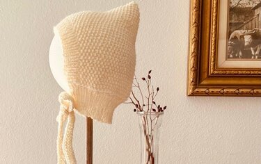 Gestrickte cremeweiße Babymütze mit Bindebändern auf Kopfmodell