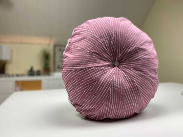 Rundes rosa Zierkissen mit weißen radialen Streifen und mittigem Knopf