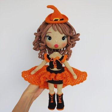 Crocheted amigurumi witch doll with orange pointed hat, ruffled skirt and black boots.