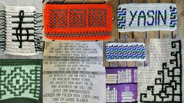 Collage aus gehäkelten Musterproben mit geometrischen Formen, einem gehäkelten Schriftzug 'YASIN' und einer eingearbeiteten Textpassage in verschiedenen Farben.