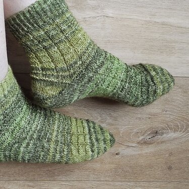 Handgestrickte grüne Socken mit Rippenmuster auf Holzboden