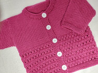 Rosafarbene handgestrickte Babystrickjacke mit weißen Knöpfen und Lochmuster