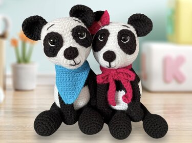 Zwei gehäkelte Amigurumi-Pandas, einer mit blauem Halstuch, einer mit pinkem Schal und Schleife
