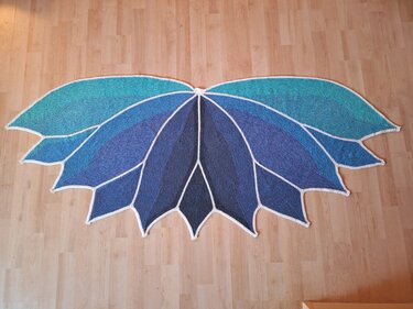 Halbrundtuch mit blauen und türkisfarbenen Blattsegmenten, weiße Einfassung, auf hellem Holzfußboden ausgebreitet