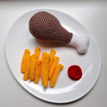 Handmade crocheted chicken drumstick, fries, and ketchup on a white plate