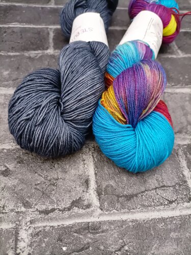 Zwei Stränge Strickgarn auf Stein, dunkelblau und mehrfarbig.