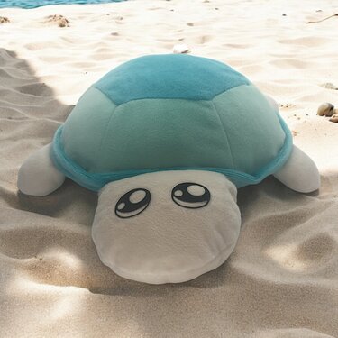 Türkise Plüsch-Schildkröte mit großen Kulleraugen auf hellem Sand