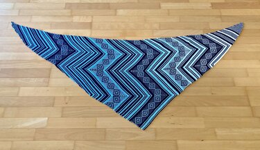 Gestricktes Dreieckstuch mit Chevron- und Rautenmuster in Blau, Türkis und Weiß, flach auf Holzboden