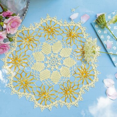 Rundes gehäkeltes Deckchen in Creme und Gelb mit sternförmigen Blumenmotiven auf blauem Untergrund