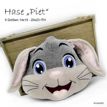 Gestickter Hasenkopf mit blauen Augen, rosa Nase und großen Ohren vor einer Holzkiste