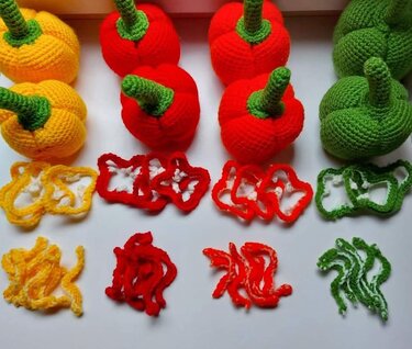 Yellow, red and green crocheted bell peppers with matching crocheted rings and strip slices on a white background.