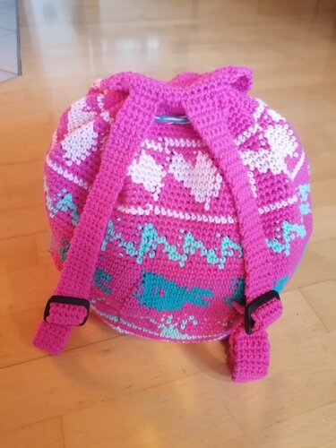 Runder gehäkelter Rucksack in Pink mit Tunnelzugverschluss, verstellbaren breiten Trägern und weißen Herz- sowie türkisfarbenen Zickzackmustern