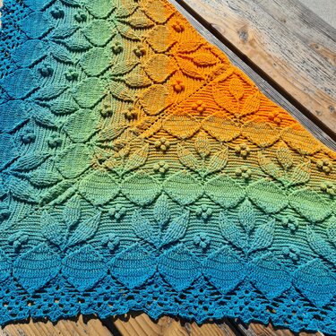 Gehäkeltes Dreieckstuch in Blau-Grün-Gelb-Orange mit Blättermuster und Spitzenkante auf Holz
