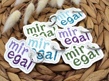 Wei
se ITH-Schl
sselanh
nger mit gesticktem Schriftzug
mir egal
in Gr
n, Hellblau und Lila auf geflochtenem Untergrund und getrockneten Gr
sern.