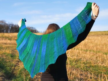 Person holding a blue and green striped crescent shawl, seen from behind.
