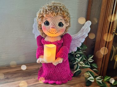 Amigurumi-Engel mit weißen Flügeln, rosa Kleid und leuchtender Kerze als Detailansicht