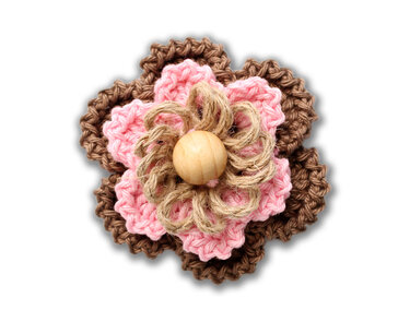 Gehäkelte Blume in Braun und Rosa mit Jute und Holzperle vor weißem Hintergrund.