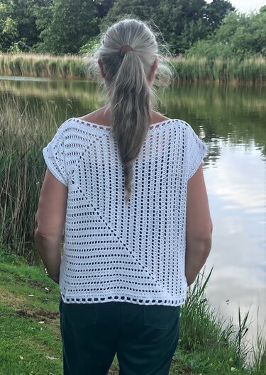 Rückenansicht einer Frau am See, trägt weißes gehäkeltes Top mit diagonalem Muster und kurzen Ärmeln
