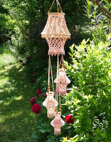 Mehrere gehäkelte, pastellfarbene Lampions an Kordeln mit Holzperlen, hängend im Garten