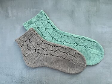 Zwei gestrickte Socken, mintgrün und grau, mit Lochmuster auf blau-grauem Untergrund