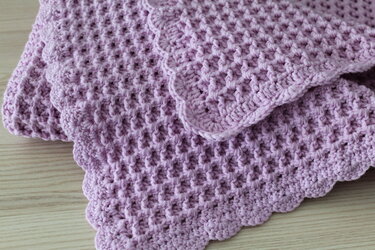 Gefaltete lavendelfarbene gehäkelte Babydecke mit Lochmuster und Muschelrand auf Holz