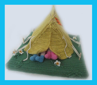 Yellow crocheted teepee on a green mat with small white flowers and blue and pink amigurumi feet inside.